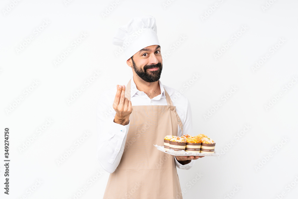 Young man holding muffin cake over isolated white background making money gesture Young man holding muffin cake over isolated white background making money gesture