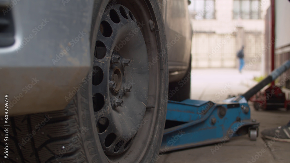 Fototapeta premium Mechanic in a vehicle workshop lifting a car on a jack