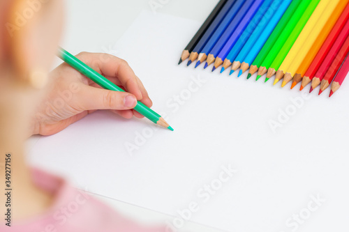 Kid girl is drawing with color pencils on white sheet of paper. Copy space for text. Mockup. Selective focus.