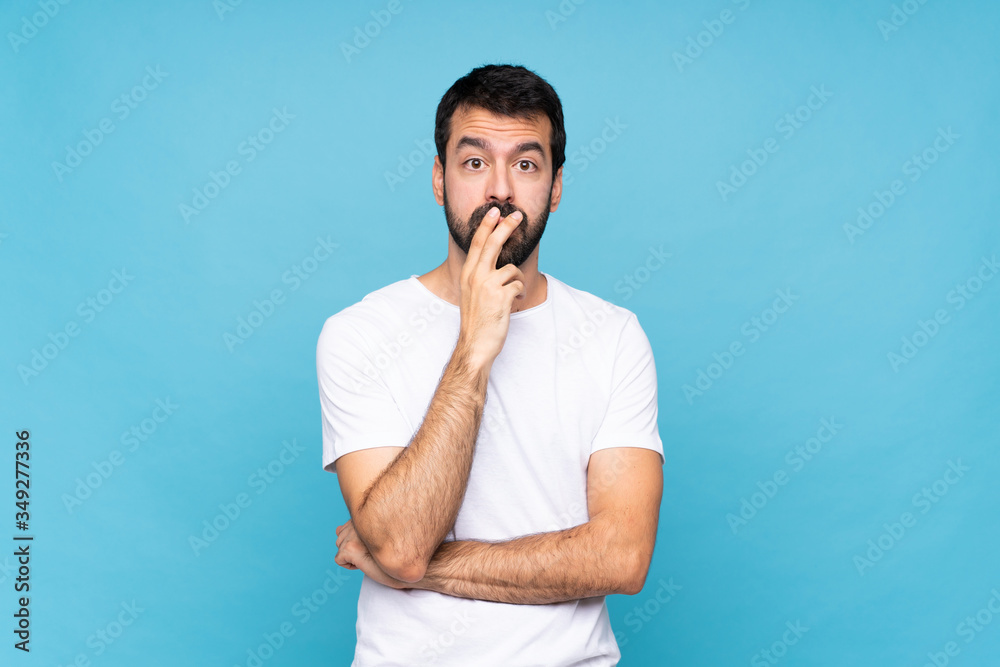 Young man with beard over isolated blue background surprised and shocked while looking right Young man with beard over isolated blue background surprised and shocked while looking right