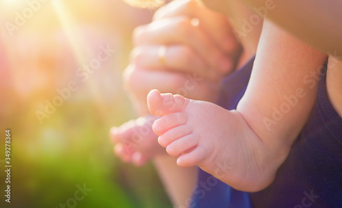 Foot barefoot toddler closeup. Toddler is sitting at his father's neck on the background of soft sunlight and blurred green bokeh. Concept father's day, family day. Family walks in the park.