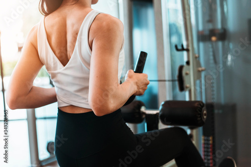 Close up back of young woman in sportswear working out with machine in gym