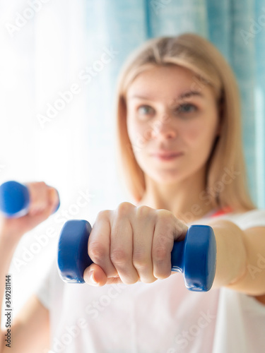 Focus on dumbbells. Woman exercising with dumbbells at home. Blured face