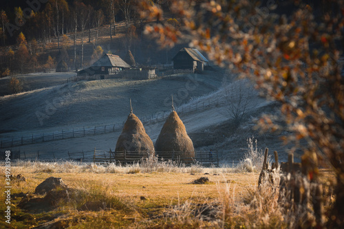 Frosty autumn morning in the village of shepherds Fundatura Ponorolui, Transilvania, Romania. Rural landscape with wooden houses and haystacks photo