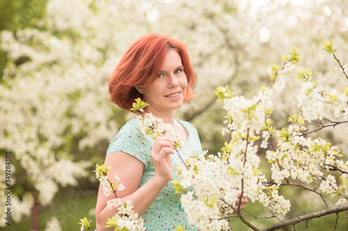 Beautiful young red hair woman in blue dress posing under apple tree in blossom 