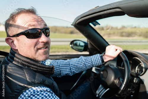 Middle-aged man enjoys free time driving his favorite cabrio car.