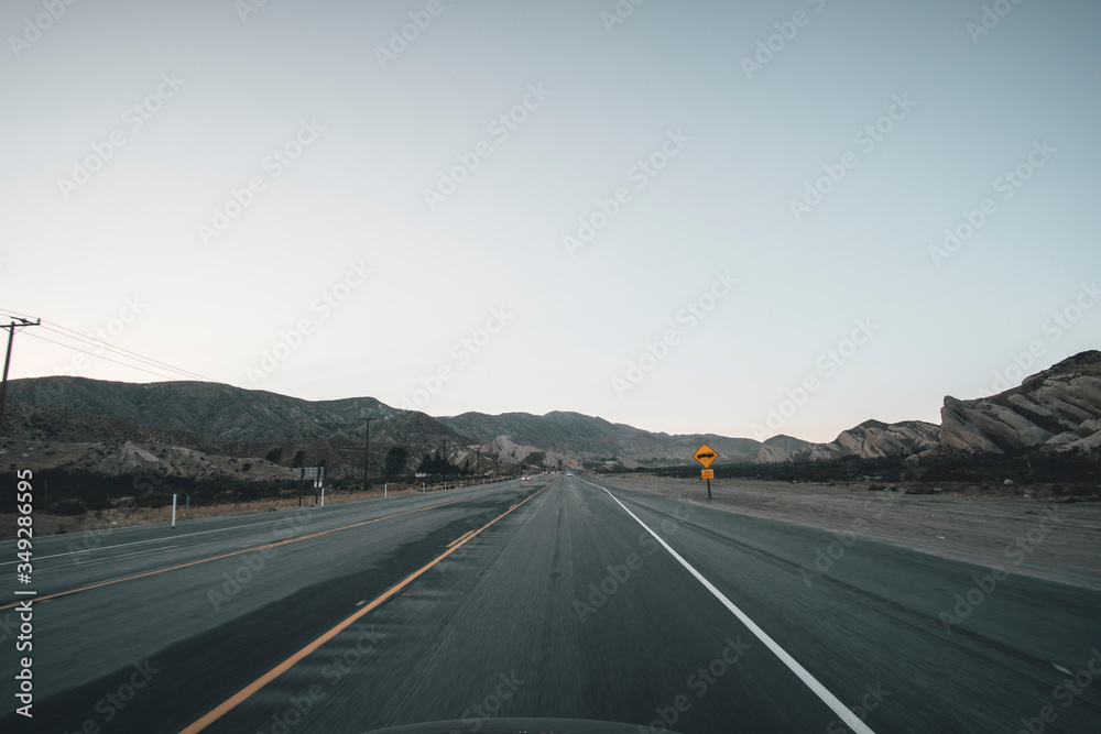 Empty Highway in California Right after Sunset with Yellow Road Sign and Mountains in the distance during Coronavirus Pandemic