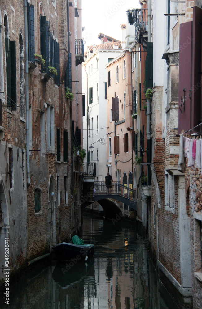 Photo of canal in Venice with historical facades ,man on the bridge and boat in the evening.