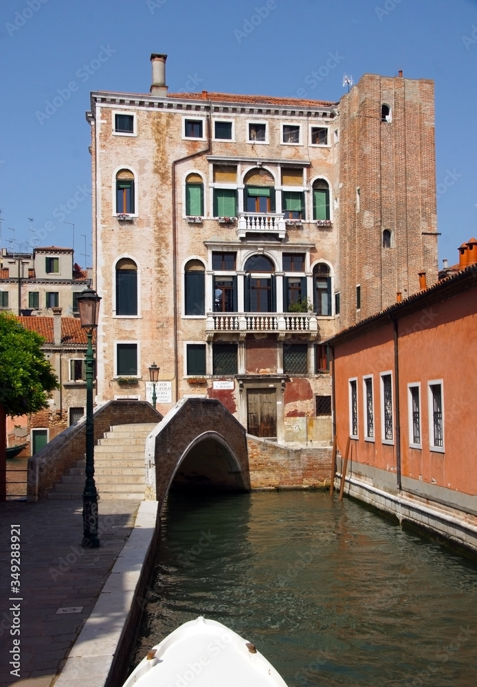 Photo of canal in Venice with historical facades with balustrades, greenery, lantern and bridge.