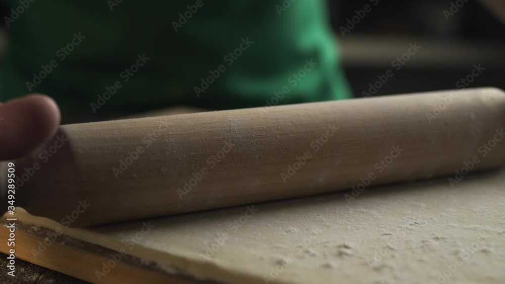 chef rolls out the dough with a rolling pin on the kitchen table