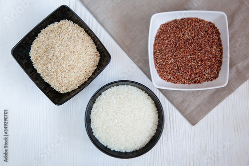 Different types of rice in cups on the table. White, brown and red.
