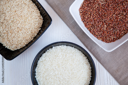 Different types of rice in cups on the table. White, brown and red.