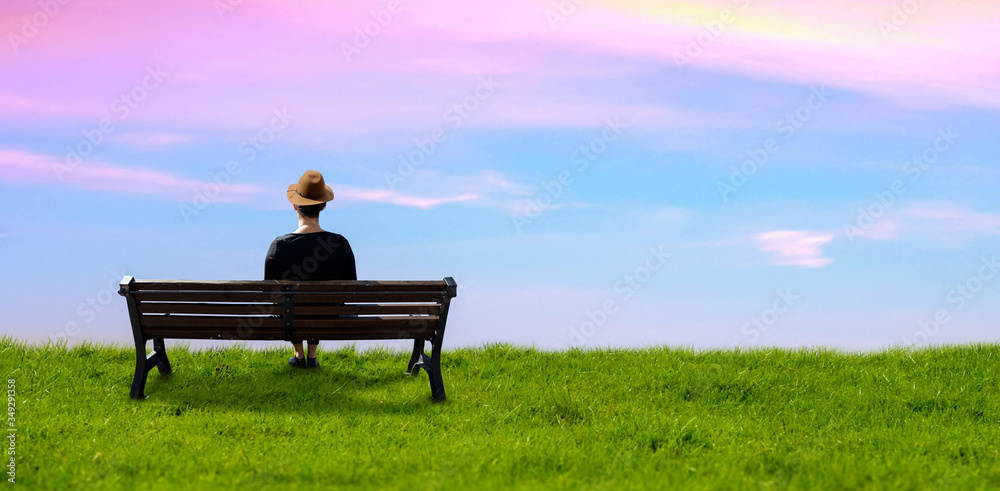 a hat wear girl sitting on a bench in a meadow green grass background sky. a hat wear girl sitting on a bench in a meadow green grass background sky.