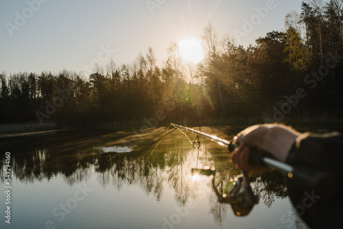 A fisherman with a fishing rod in his hand catches a fish on the shore of a lake or river. Fishing Day. Spinning in hand on pond background.