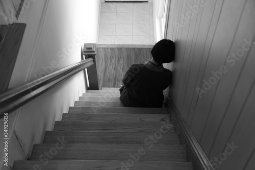Woman sitting alone sadly on wooden staircase, leaning her head against the wall, back view, white tone