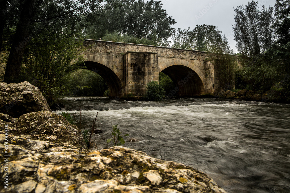 Puente desde la orilla del río un día nublado en larga exposición.