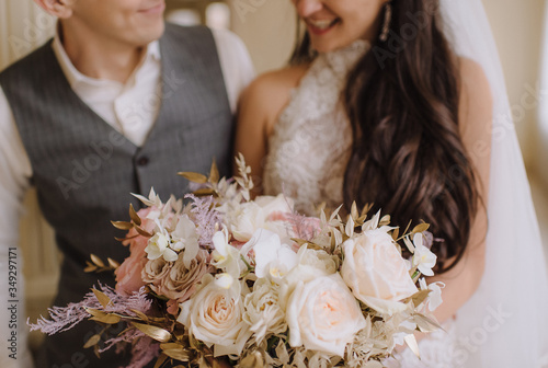 Close-up of a bride's bouquet of peach roses, carnations, golden leaves of eucalyptus. The bride in a white dress with long sleeves holds a bouquet in her hands. 