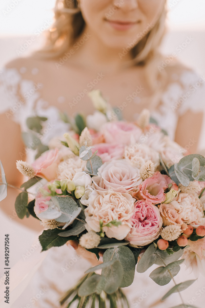 Naklejka premium Close-up of a bride's bouquet of peach roses, carnations, eucalyptus. The bride in a white dress with long sleeves holds a bouquet in her hands. 
