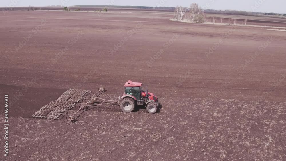 Aerial view tractor cuts furrows in farm field for sowing farm tractor with rotary harrow plow preparing land for sowing. Tractor with harrows prepares the agricultural land for planting crop Aerial view tractor cuts furrows in farm field for sowing farm tractor with rotary harrow plow preparing land for sowing. Tractor with harrows prepares the agricultural land for planting crop