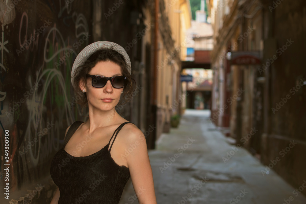 Beautiful style young woman wearing hat and in the city street in front of the old brick wall. Fashion tourist street concept. Outdoor fashion photo of young beautiful lady in hat and dress. Summer