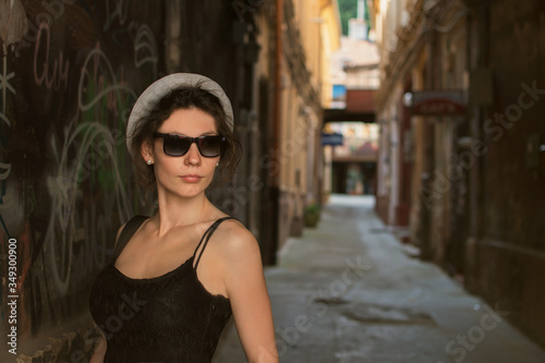 Beautiful style young woman wearing hat and in the city street in front of the old brick wall. Fashion tourist street concept. Outdoor fashion photo of young beautiful lady in hat and dress. Summer