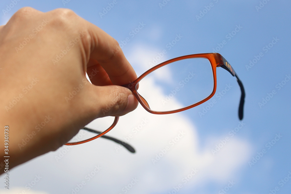 Hand holding glasses and raised upward cloudy blue sky Hand holding glasses and raised upward cloudy blue sky