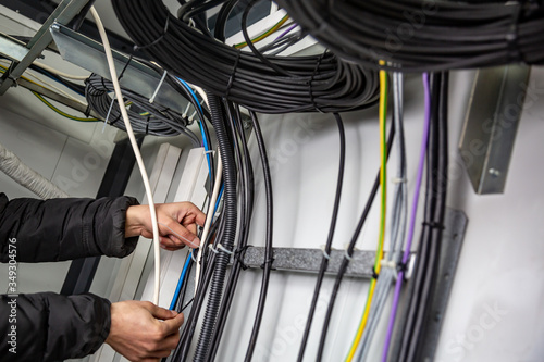 Hands fasten the cable ties on the cable, which are on the cable tray. Horizontal orientation.