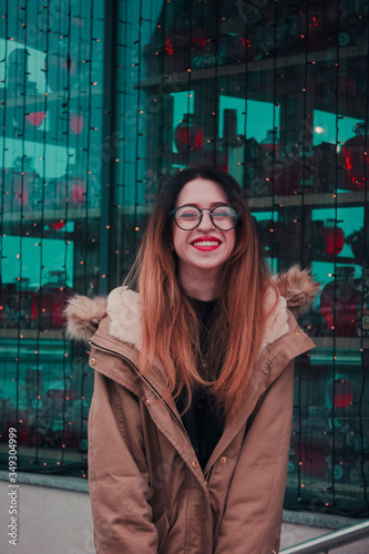 Confident successful business woman in glasses with red lipstick on a blue glass background with a garland © Тамара Печеная