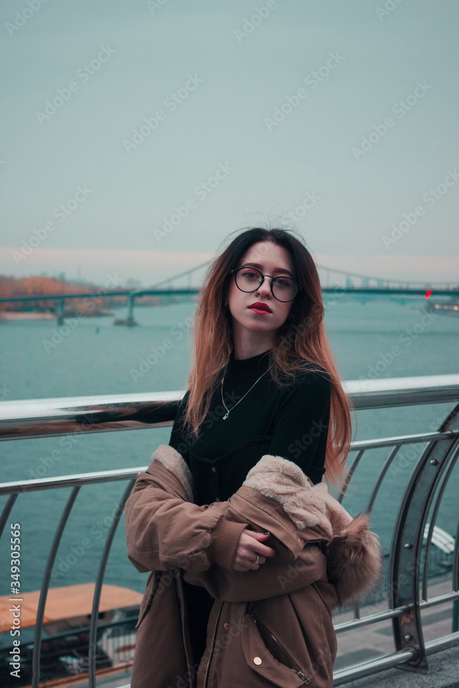 Pensive business woman looks into the distance on the background of the river and the bridge. Girl dressed in black and glasses. Business style. Woman with red lipstick