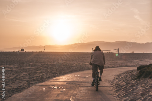 Man riding a bike down Santa Monica beach watching the sunset 