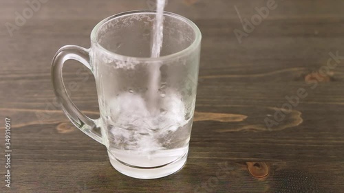 Pour hot water into a transparent empty glass on a wooden table. Bubbles, steam and splashes