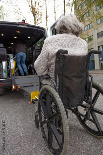 Handicapped person loading in a wheelchair into a minibus for transportation.
Male driver and elderly woman in medical masks.