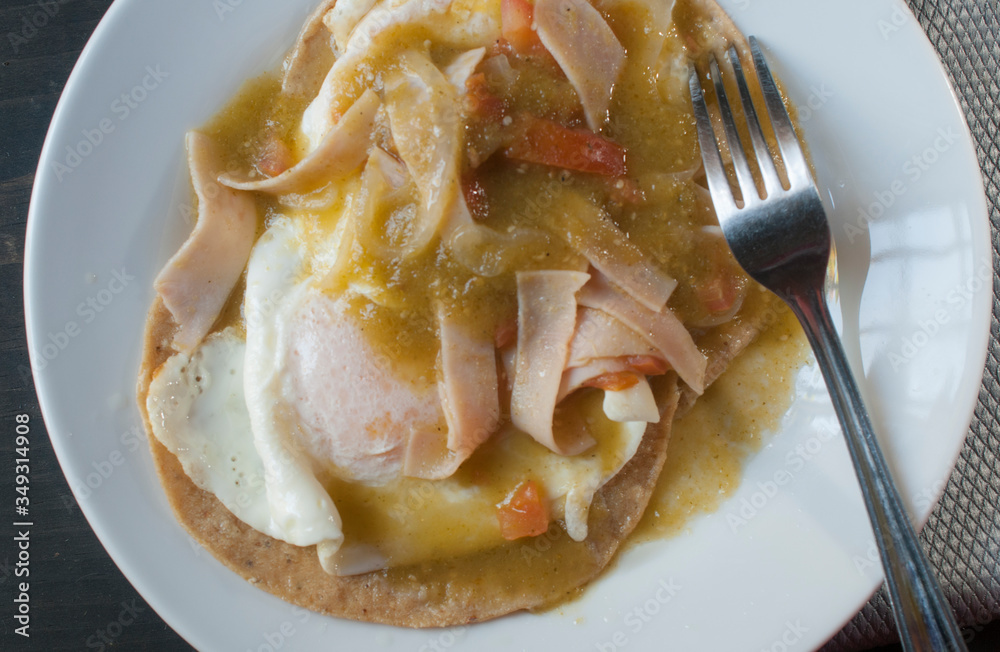 Φωτογραφία Top view of Huevos Rancheros or Ranch eggs on a white plate and a fork on the side with spicy green salsa ham and chili, on top of corn tortillas Mexican breakfast concept