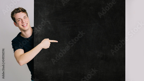 Young blue-eyed boy on an isolated white background shows a customizable billboard with text with his index finger. Space for text, customizable text.