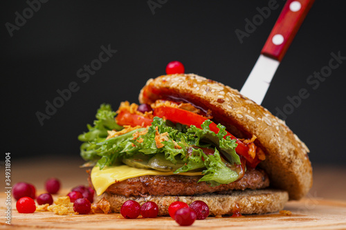 Delicious juicy burger with beef patty  bun  cranberry sauce and vegetables on a serving wooden board on a black background. Food delivery. Fast food restaurant.