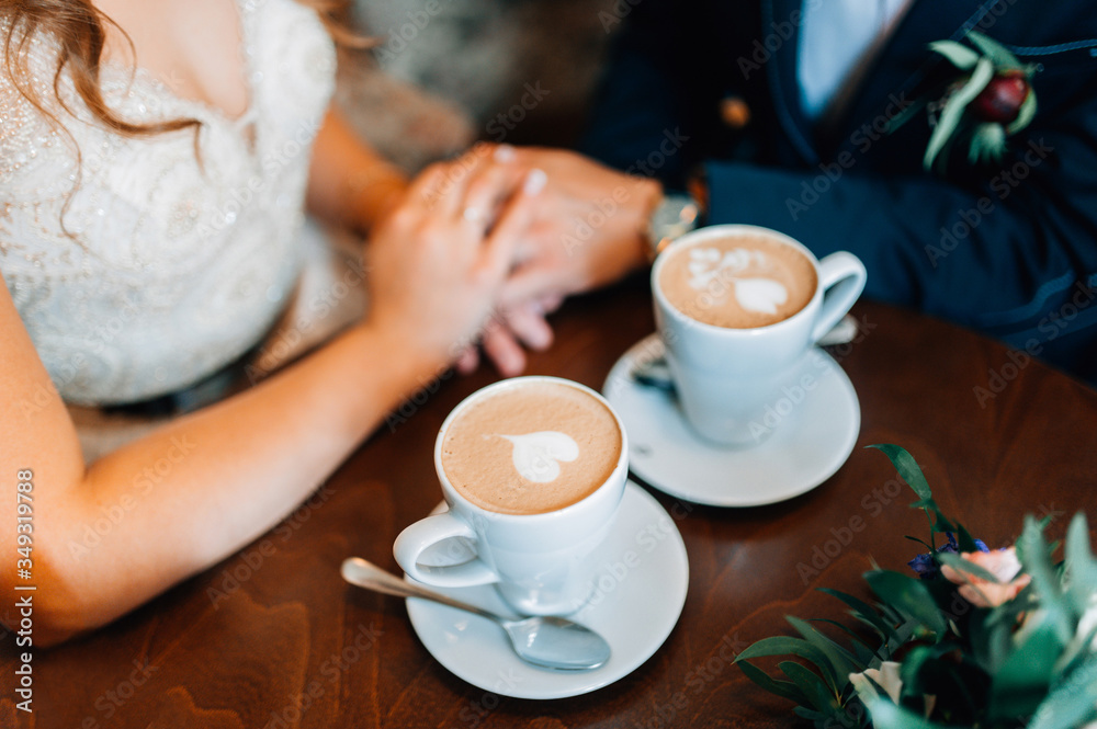 Bride and groom holding hands together. Romantic moment. Coffe cups with hearts Bride and groom holding hands together. Romantic moment. Coffe cups with hearts