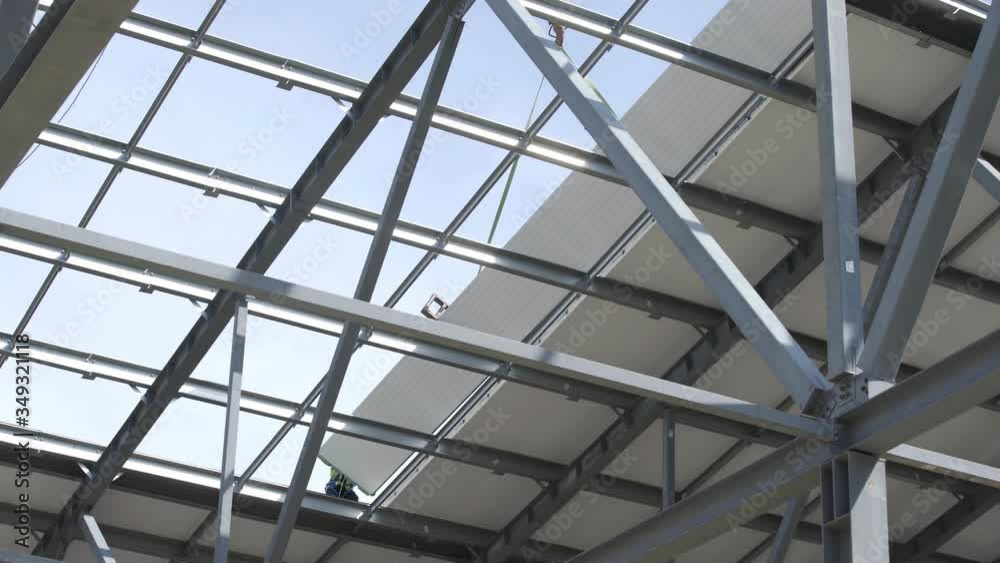 Modern storehouse construction site, structural steel structure of new commercial building against. Construction of modern factory or warehouse. Crane lowers roofing. Man working on roof Modern storehouse construction site, structural steel structure of new commercial building against. Construction of modern factory or warehouse. Crane lowers roofing. Man working on roof