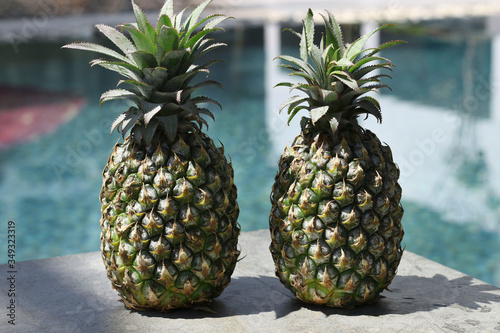 Two ripe pineapples on the edge of the pool with water. Concept of summer holidays in tropical countries.