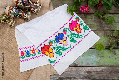 Fototapeta Naklejka Na Ścianę i Meble -  Handmade embroidery towel on a vintage wooden table with geranium flower and ceramic jugs
