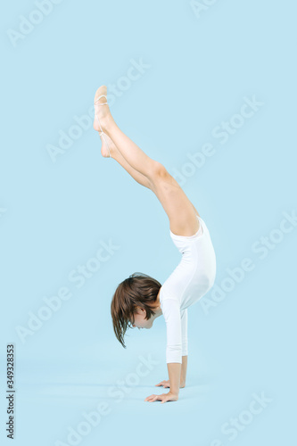 Fit little girl in a white leotard doing handstand over blue background photo