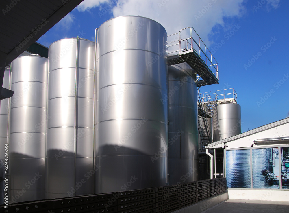 Large metallic glossy tanks with an observation deck at an outdoor plant on a sunny day