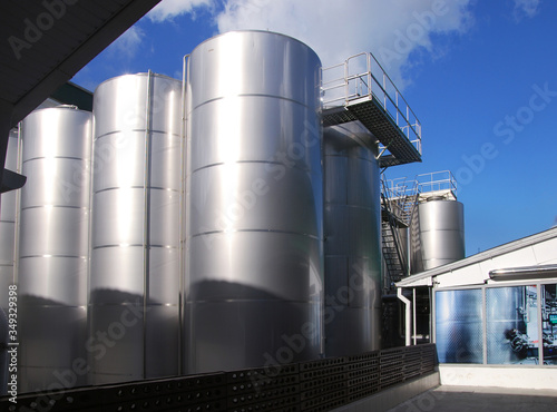 Large metallic glossy tanks with an observation deck at an outdoor plant on a sunny day
