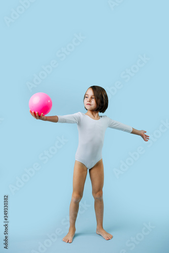 Little girl in a white leotard with gymnastic ball over blue photo