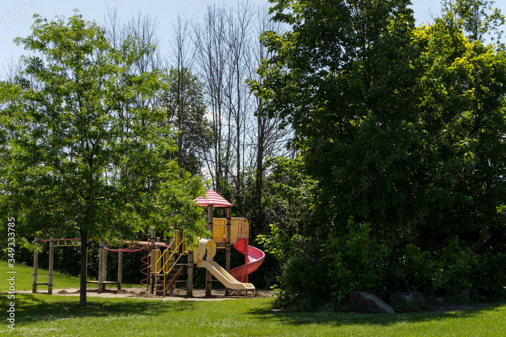 Play structure in a schoolyard park, surrounded by tall green trees, with slides and monkey bars