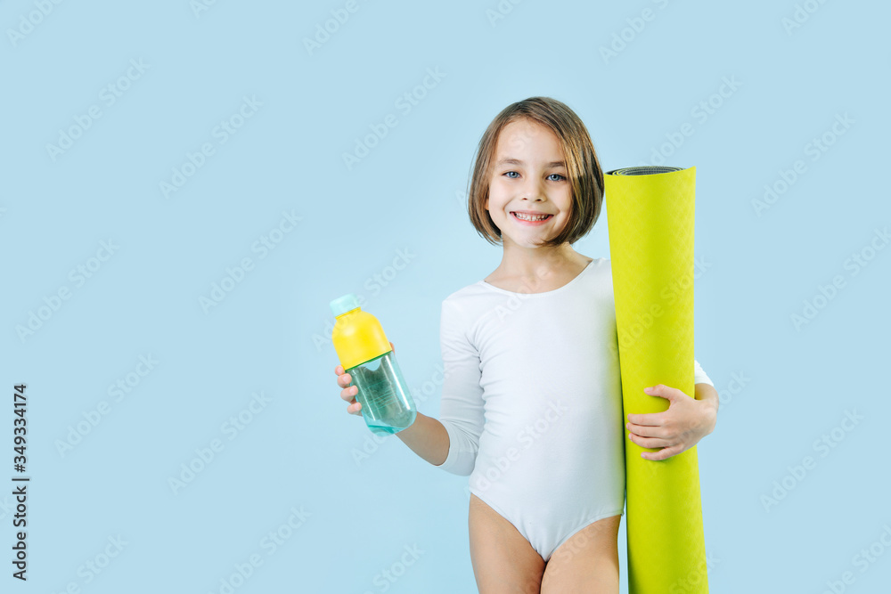 Happy smiling girl in a white leotard with rolled mat and water bottle over blue Happy smiling girl in a white leotard with rolled mat and water bottle over blue