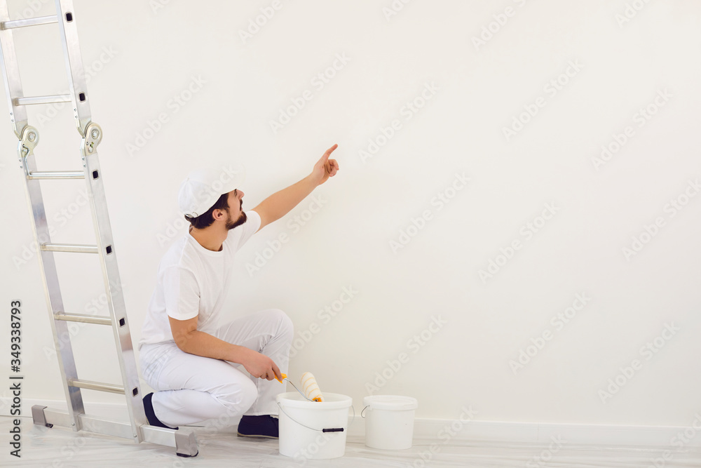 A painter in white uniform points to a white background for painting in the room. A painter in white uniform points to a white background for painting in the room.