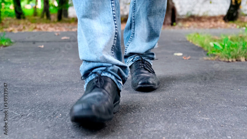 View of man's walking legs in blue jeans, black leather shoes.