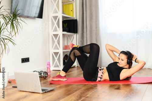 Get in shape at home. A woman is training with a video classes, she is watching workout video tutorial on laptop and doing abdominal crunches
