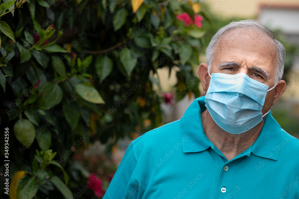 Foto Stock Ritratto di uomo anziano con mascherina protettiva e Polo  azzurra nel giardino di casa sua