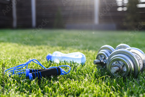 Workout in the backyard. Iron dumbbells, sports bottle of water and jump rope on the greenlawn photo